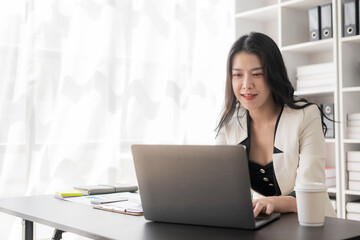 Portrait of an Asian businesswoman in a formal suit working with a laptop in a modern office, human resources and small business owner, businessman concept, financial accounting.