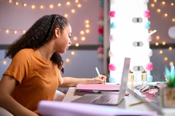 Teenage Girl At Home In Bedroom Studying Using Laptop Computer