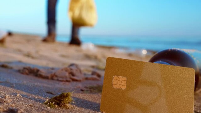 The image of a credit card on the sand and a person collecting plastic waste symbolizes a shift towards sustainable consumption and choosing environmentally responsible options. Plastic Waste