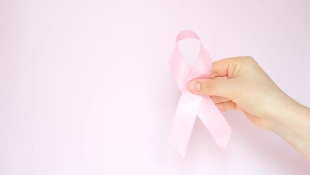 Female hand holding a ribbon on pink background close-up.