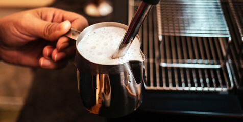 Close-up of Barista hand using high-pressure steam-operated milk frother to prepare a cappuccino coffee milk