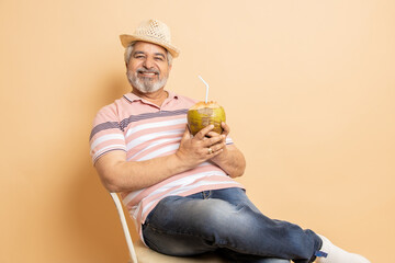 Retired senior indian man casual cloths and hat drinking coconut water while sitting on chair...