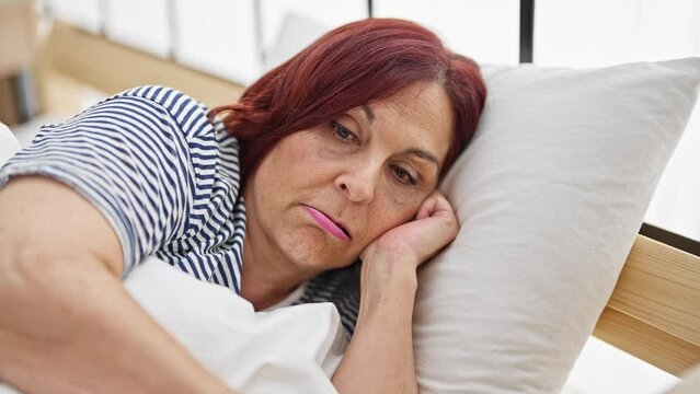 Middle age woman lying on bed with serious face at bedroom