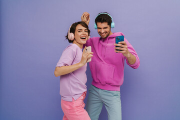 Young couple dancing while listening music with headphones and mobile phones isolated over purple background