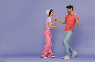 Young cheerful man and woman dancing isolated over purple background