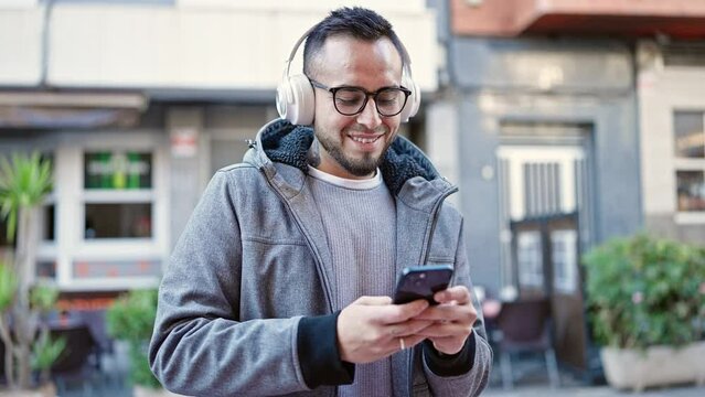 Hispanic man smiling confident listening to music using smartphone at street
