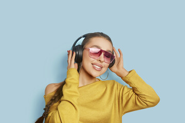 Beautiful girl singing favorite song, listening to music in wireless headphones, smiling and dancing, standing over blue background