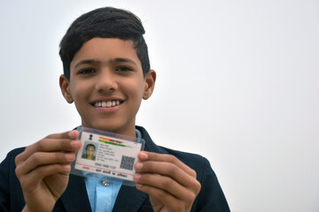 Indian school boy wearing dark blue school uniform, with smiling face shows her blurred aadhar card...