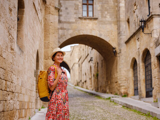 Fototapeta na wymiar summer trip to Rhodes island, Greece. Young Asian woman in ethnic red dress walks Street of Knights of Fortifications castle. female traveler visiting southern Europe. Unesco world heritage site.