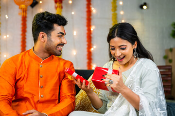 surpised indian young sister by receiving gift from brother during raksha bandhan festival celebration at home - concept of tradition culture, Sibling Bonding and Rakhi Gifting