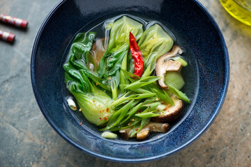 Vegetable soup with bok choy and shiitake mushrooms in a dark-blue bowl, middle close-up, high angle view - obrazy, fototapety, plakaty
