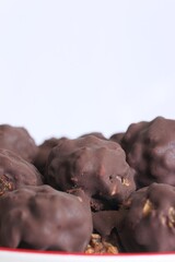 Homemade candy made from nuts and dried fruits. Some are covered in chocolate. They lie on a plate. Close-up.