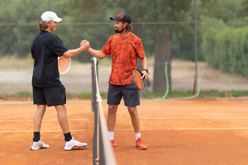 Friendly tennis match - opponents shake hands above the net