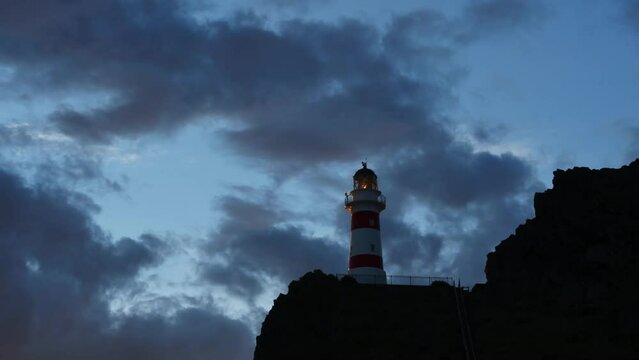 time lapse of a white and red lighthouse on a rocky hill against a dramatic cloudy sunset sky.