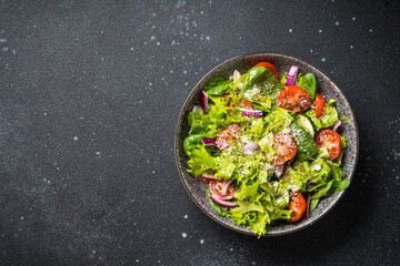 Green vegetable salad with fresh leaves at black background. Top view.