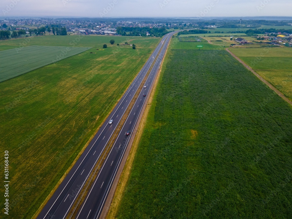 Poster aerial view of a large green field, with a single road running through it, surrounded by trees