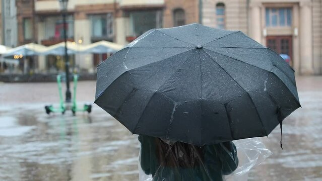 A woman with a black umbrella walks through the city in rainy weather.