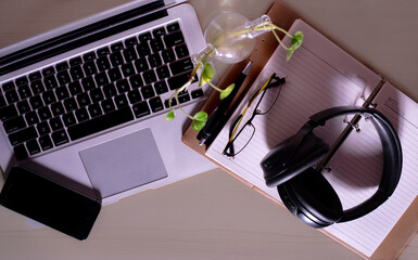 Top view of office Workplace with open laptop, a blank open note book, a smart phone ,a pen, a specs and a head phone on a wooden desk