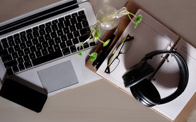 Top view of office Workplace with open laptop, a blank open note book, a smart phone ,a pen, a specs and a head phone on a wooden desk