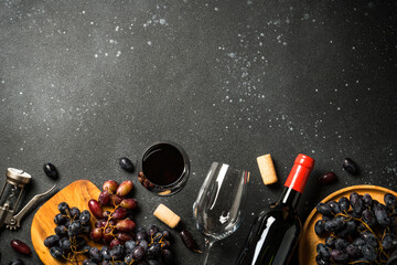 Red Wine at black background. Glass of wine, bottle, crape and corkscrew. Top view with copy space.
