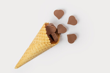 A waffle cone full of heart-shaped chocolates isolated on a pink background, top view. Sweet food. Valentine card