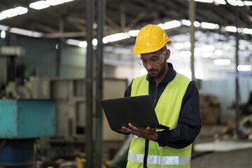 Male engineer worker working with laptop computer for control machine in factory. Male worker working with CNC machine with safety uniform, helmet in industry factory