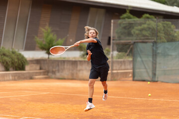 A boy teenager in black t-shirt playing tennis on the court - frame in motion - hitting back the...