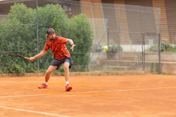 An adult man in red t-shirt playing tennis on the court