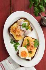 Open sandwich or smorrebrod with rye bread, herring, eggs, caramelized onions, parsley and cottage cheese on old wooden rustic table backgrounds. Danish or Scandinavian traditional food snack lunch.