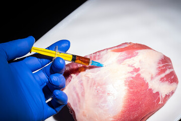 Injection from a syringe into raw meat on a dark background.Conceptual illustration of hormones and antibiotics in food production.