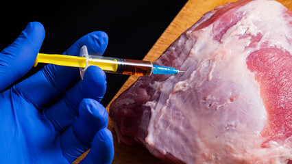 Injection from a syringe into raw meat on a dark background.Conceptual illustration of hormones and...