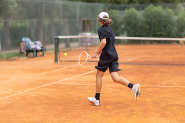 A boy teenager in a black t-shirt running on the tennis court to hit back the ball