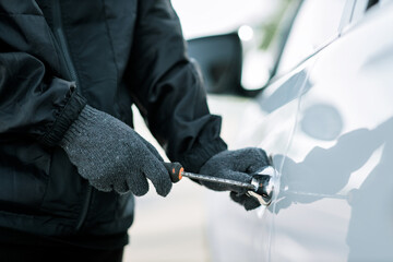 Man dressed in black holding screwdriver to break lock and steal a vehicle on the road, Social destruction, Insurance, Car thief concept.