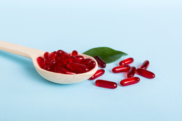 Vitamin capsules in a spoon on a colored background. Pills served as a healthy meal. Red soft gel...