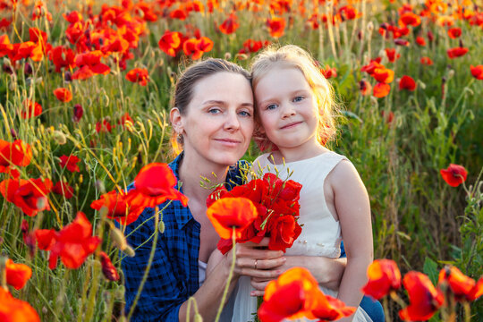 Little girl and her mother with a bouquet of poppies in a field on a summer day