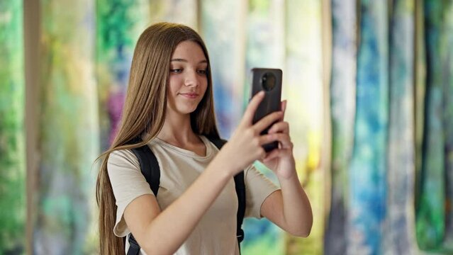 Young beautiful girl student wearing backpack make photo by smartphone at art gallery