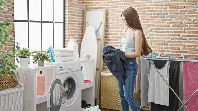 Young beautiful girl throwing clothes on washing machine at laundry room