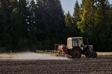 Agricultural field, crop sprayer attached to farm tractor applies herbicides to crops.