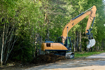 Crawler excavator deepens storm ditch on country road.
