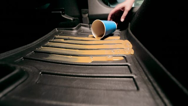 Spilled coffee on the carpet in the car. Pollution of the car in the cabin. A blue disposable cup with coffee falls on the car floor mat