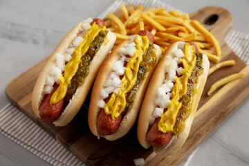 Homemade Deep Fried Hot Dogs with Mustard, Onion and Pickle Relish on a wooden board, side view.