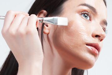 Young brunette woman applying moisturizing gel mask with brush on her face