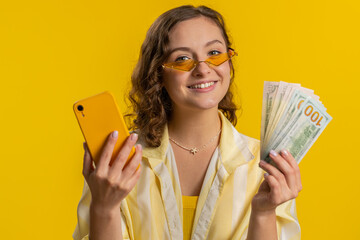 Young woman looking smartphone display sincerely rejoicing win, receiving money dollar cash...