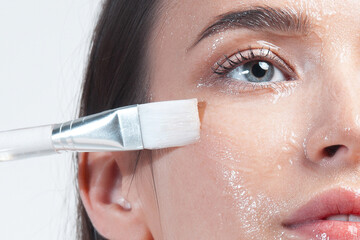 Beautiful young white woman applying cleansing gel to her facial skin using brush
