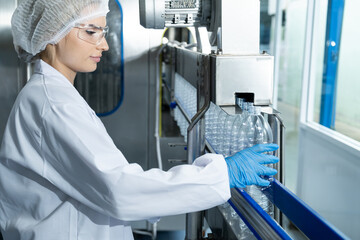 Caucasian women scientist with lab cote inspect quality of drinking water inside of the production line factory while using digital tablet to check cleanliness and standard, quality assurance