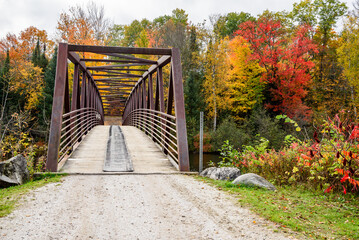 Empty steel pedestrian and bicycle bridge spanning a river with forested banks at the peak of fall foliage