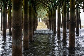 Sun shining through a pier at Myrtle Beach, SC as the surf rolls in