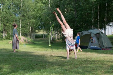Caucasian girl doing stunts on green grass of a campsite, against her family