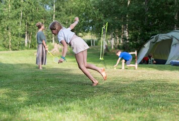 Caucasian girl doing stunts on green grass of a campsite, against her family