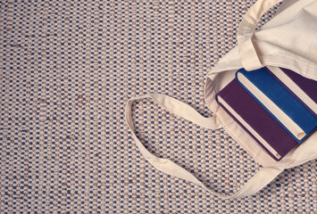 Clever weighty books in textured blue and lilac fabric covers lie in an open linen bag on a natural...